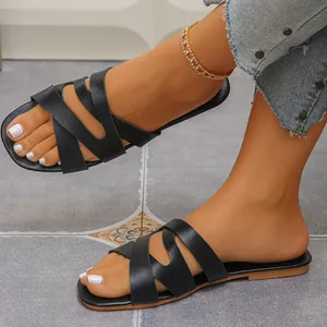 Close-up of stylish black open-toe flat sandals with cross straps worn on feet.