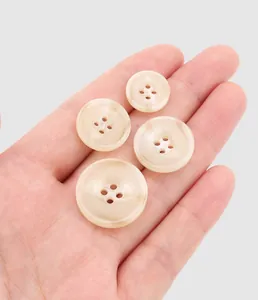 Close-up detail of premium beige resin buttons in various sizes held in hand for scale comparison