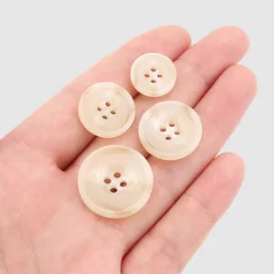 Four assorted sizes of cream resin four-hole buttons displayed on a palm for scale