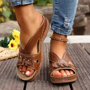 Detalle de sandalias con cuña marrones con apliques florales y diseños cortados con láser