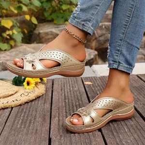 Primer plano de sandalias de cuña doradas para mujer con flores en una plataforma de madera