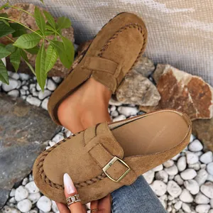 Close-up detail of tan suede mules with metal buckle and decorative stitching