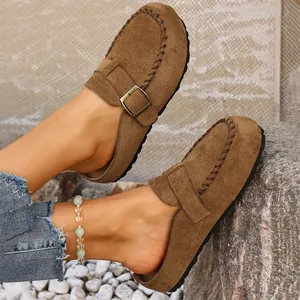 Close-up of stylish brown suede buckle clogs worn with denim jeans and a beaded anklet