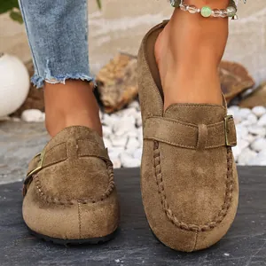 Close-up of brown suede clogs with decorative buckle strap and stitched detailing