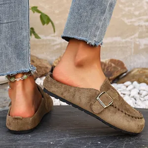 Close-up detail of brown suede closed-toe clogs with a decorative metal belt buckle.