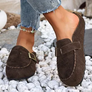 Detailed view of dark brown suede mules with metal buckle strap on white pebble background