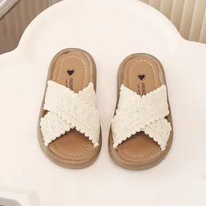 Detalle de chanclas para niña con tiras cruzadas de ganchillo crema y pompones.