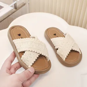 Primer plano de chanclas para niña con tiras de encaje cruzadas y pompones decorativos.