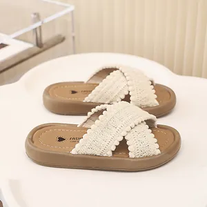 Primer plano de las tiras cruzadas de encaje crema y pompones de estas lindas chanclas de niña.