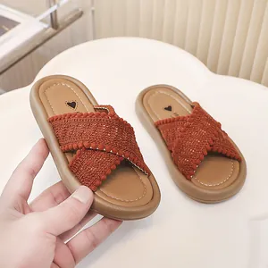 Primer plano de sandalias tejidas para niña en color terracota con bordes de pompones