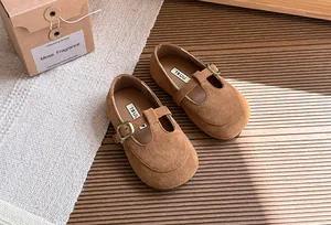 Dettaglio ravvicinato di scarpe bimba T-strap in camoscio marrone con suola morbida