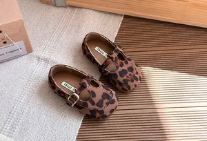 Dettaglio di scarpe T-strap per bambini con stampa leopardata, fibbia in metallo e pelle.