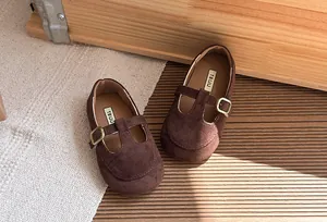 Primo piano di scarpe T-strap in camoscio marrone retrò per bambine con fibbia dorata