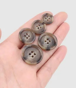 Macro detail of high-quality brown horn-patterned resin buttons held in a hand for scale