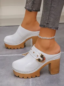 Close-up detail of white patent leather platform clogs featuring gold buckle and rivets