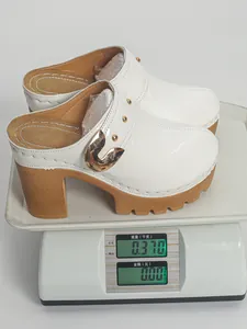 Close-up detail showing the weight of white patent leather platform clogs on a scale
