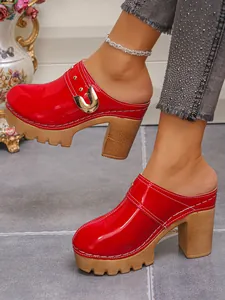 Stylish red patent leather platform clogs with gold buckle and rivet details shown on feet
