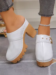 Close-up of white patent leather platform mules with chunky heels and rivets.