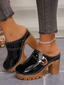 Close-up of black patent leather platform mules with gold buckle and rivet details