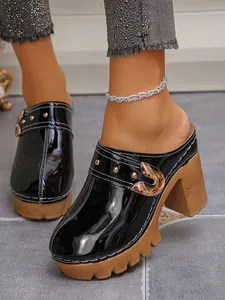 Detailed view of black patent leather mules featuring chunky high heels and metallic buckles.