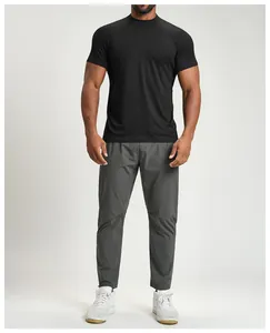 Full body view of a man wearing a black athletic short sleeve t-shirt and grey pants.