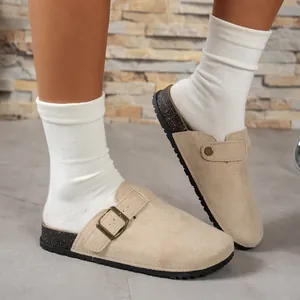Detail view of stylish beige suede clogs with adjustable bronze buckle and cork sole.