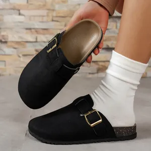Close-up detail of stylish black suede clogs featuring a gold buckle and textured cork sole