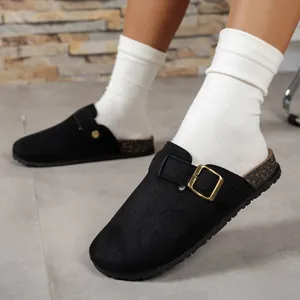 Close-up detail of black suede-textured clogs featuring gold buckle and cork sole