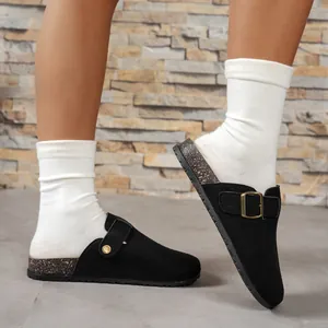 Close-up of black suede Boston clogs with metallic buckle and white socks on stone floor