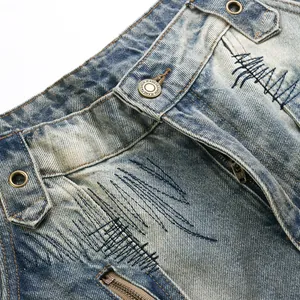 Primo piano di jeans blu stile high-street con ricami pesanti e lavaggio dirty.