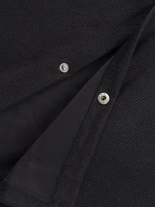 Détail du tissu gaufré noir et des boutons-pression en métal argenté sur une veste décontractée.