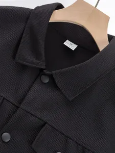 Gros plan d'une veste de travail noire à texture gaufrée avec revers et boutons mats.