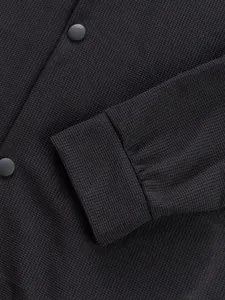 Détail du tissu gaufré noir et du bouton pression sur une veste de travail décontractée