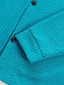 Détail de la manche d'une veste en maille gaufre sarcelle avec boutons-pression noirs