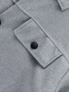 Gros plan sur le tissu gris texturé d'une veste de travail avec rabat de poche et bouton