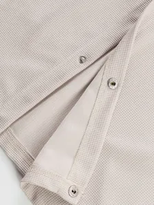 Gros plan sur le tissu gaufré beige d'une veste avec des boutons-pression en métal