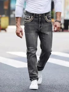 Detail of trendy men's dark grey denim jeans with unique embroidered pocket decorations.