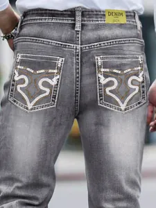 Close-up of stylish grey men's jeans featuring ornate white embroidery on back pockets