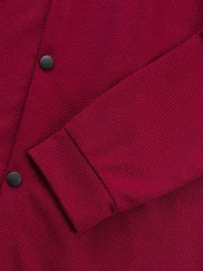 Gros plan sur le tissu gaufré bordeaux et les boutons-pression noirs de la veste