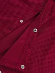 Gros plan sur un tissu gaufré bordeaux avec des boutons-pression métalliques de veste