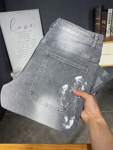 Dettaglio ravvicinato di jeans grigi lavati con design artistico a schizzi di vernice bianca
