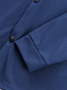 Gros plan du tissu à texture gaufre bleue et des boutons noirs mats d'une veste.