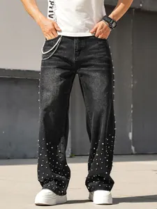 Close-up view of men's straight-leg denim jeans with rhinestone studs and pearl chain detail