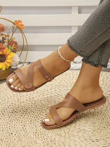 Close-up of stylish brown flat sandals with metal rivet details on woven mat