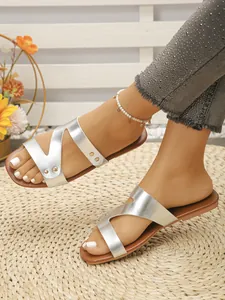 Women's silver flat slide sandals with vintage rivet details shown on woven beach mat