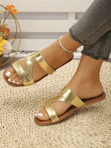 Detail shot of metallic gold flat sandals with vintage rivet decor and straw mat base