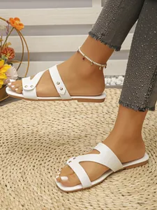Stylish white flat sandals with gold rivet detail worn on a woven straw beach mat.