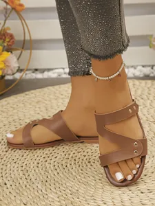 Close-up of brown women's flat slide sandals featuring Z-strap design and gold rivets.