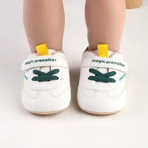 Front view detail of white baby pre-walker shoes with green laces and yellow straps