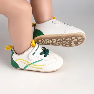 Close-up of white baby pre-walker shoes with green accents and textured anti-slip sole.